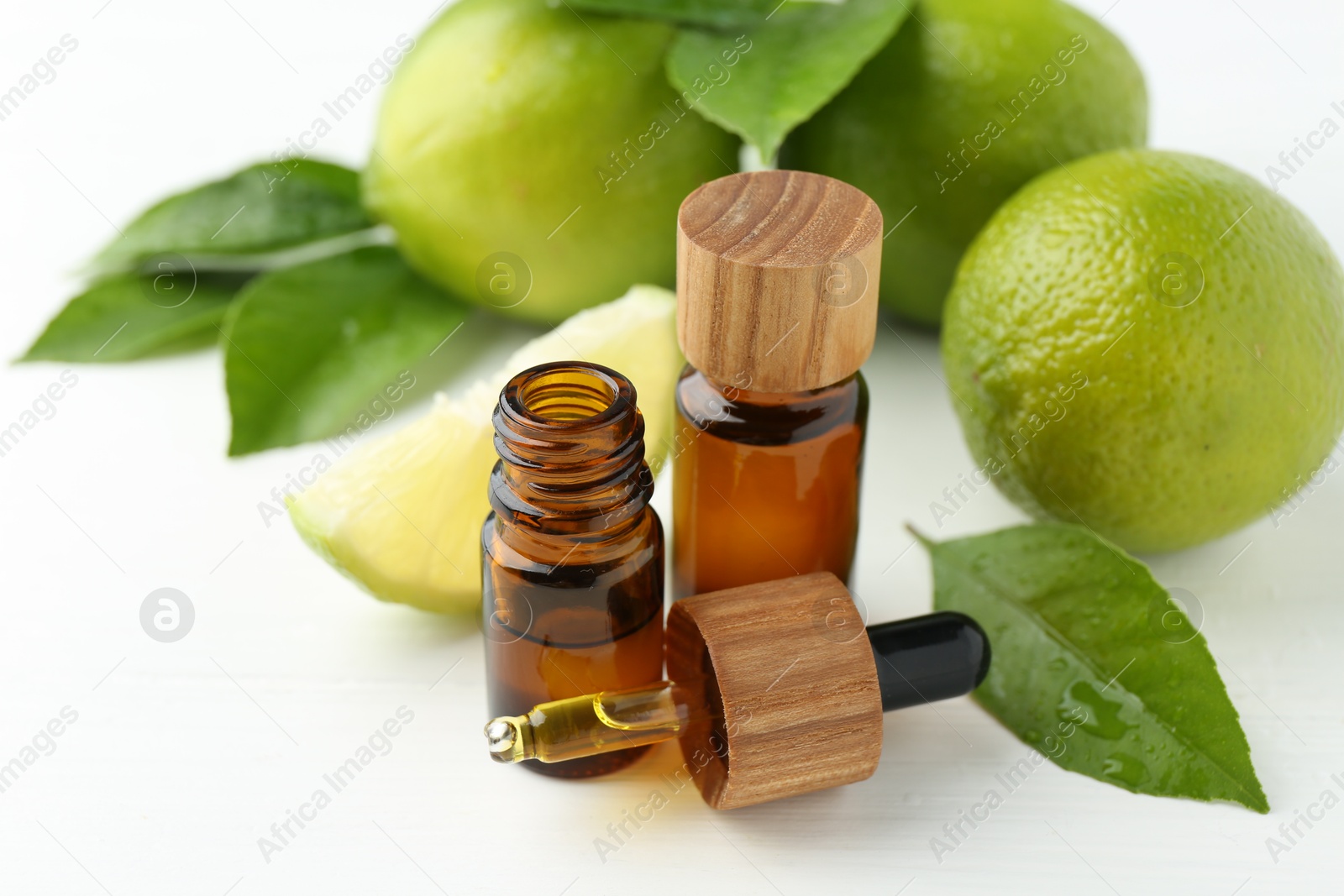 Photo of Essential oils in bottles, dropper, limes and green leaves on white table