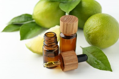 Essential oils in bottles, dropper, limes and green leaves on white table