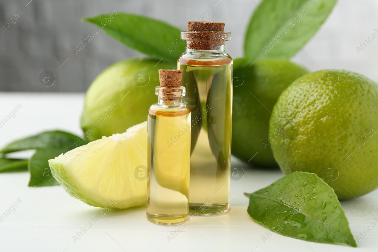 Photo of Essential oils in bottles, limes and green leaves on white table, closeup