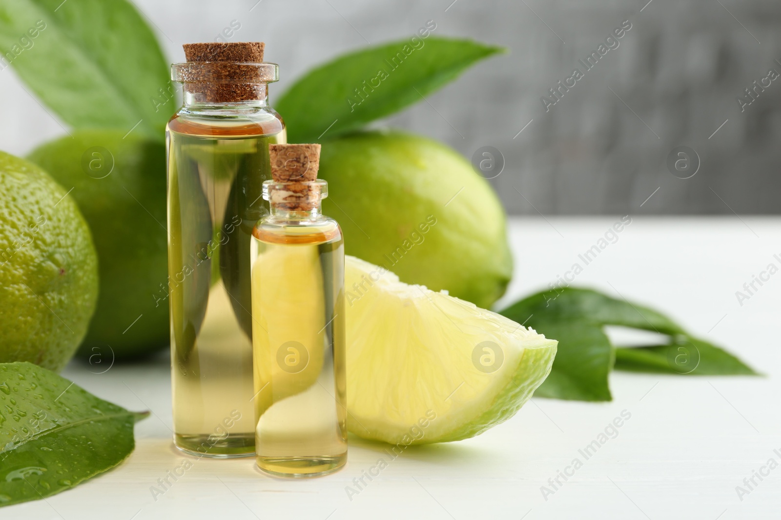 Photo of Essential oils in bottles, limes and green leaves on white table, closeup