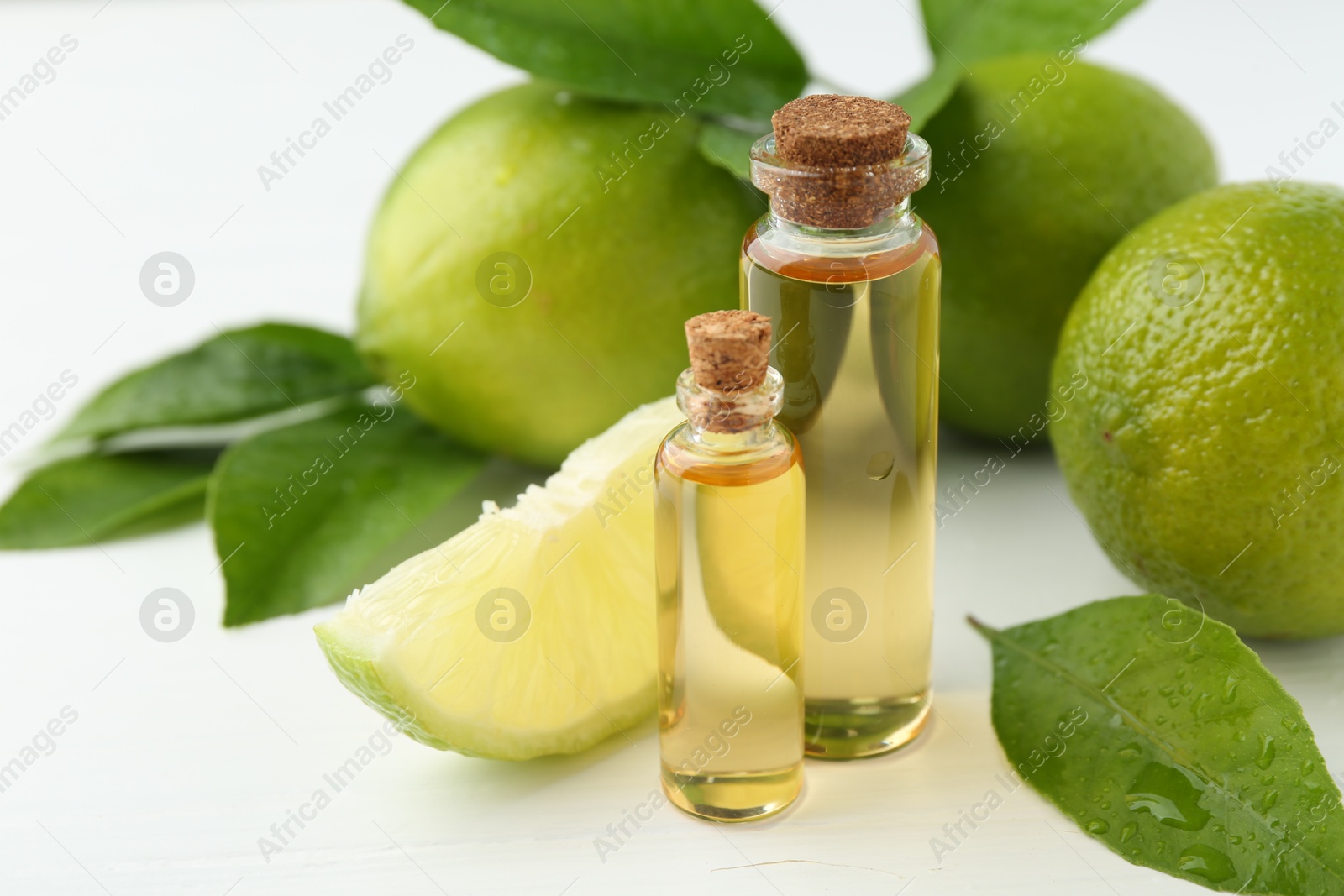 Photo of Essential oils in bottles, limes and green leaves on white table, closeup