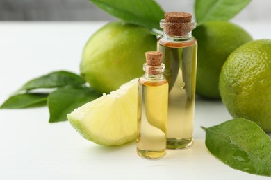 Photo of Essential oils in bottles, limes and green leaves on white table, closeup