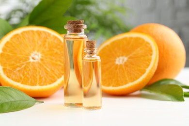 Essential oils in bottles, oranges and green leaves on white table