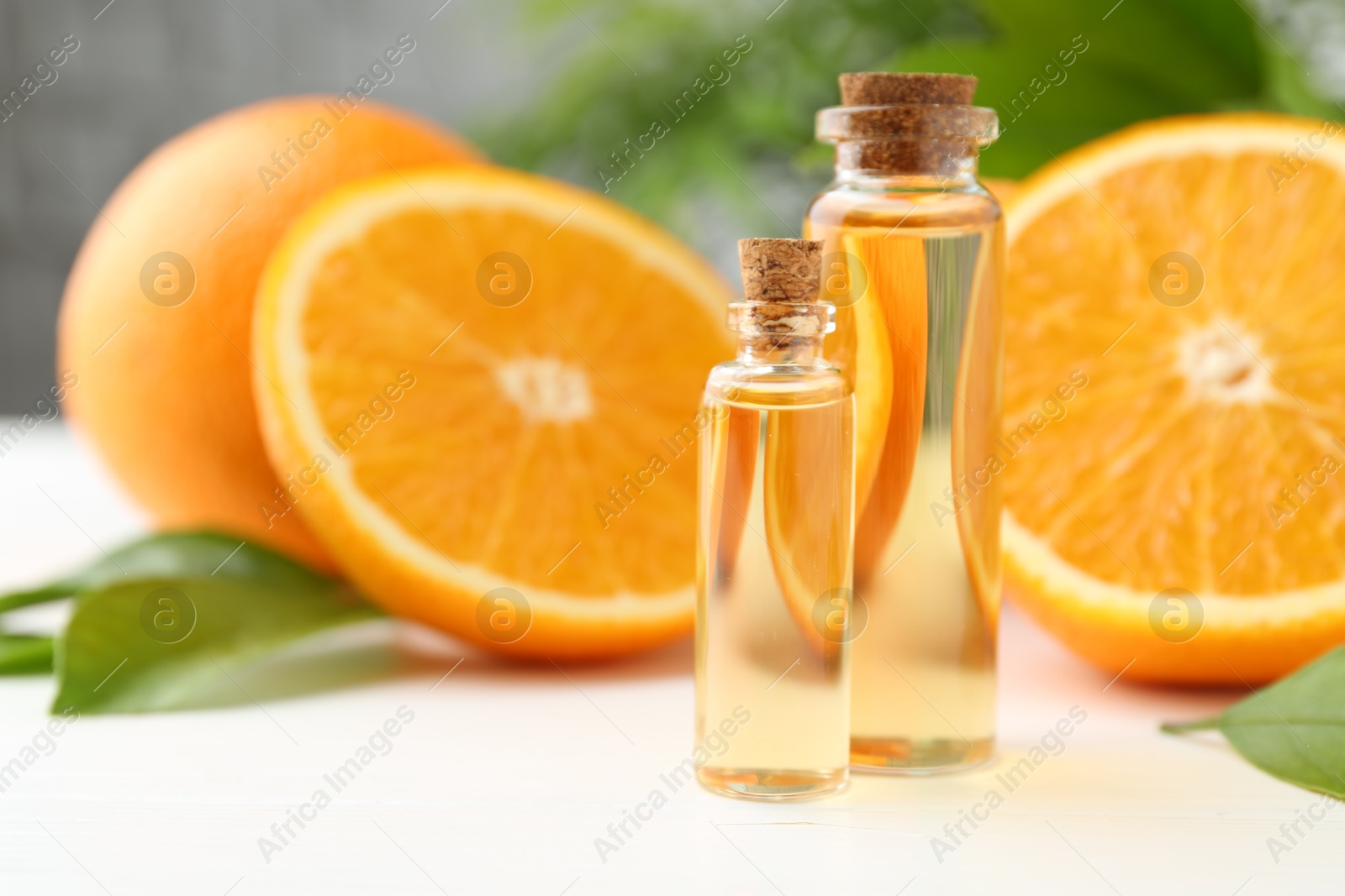 Photo of Essential oils in bottles, oranges and green leaves on white table, closeup