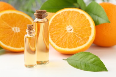 Photo of Essential oils in bottles, oranges and green leaves on white table