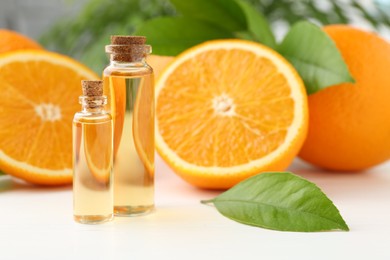 Photo of Essential oils in bottles, oranges and green leaves on white table