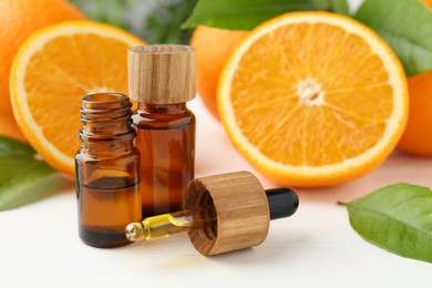 Photo of Essential oils in bottles, dropper, oranges and green leaves on white table, closeup