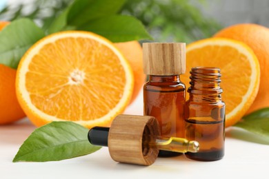 Photo of Essential oils in bottles, dropper, oranges and green leaves on white table, closeup