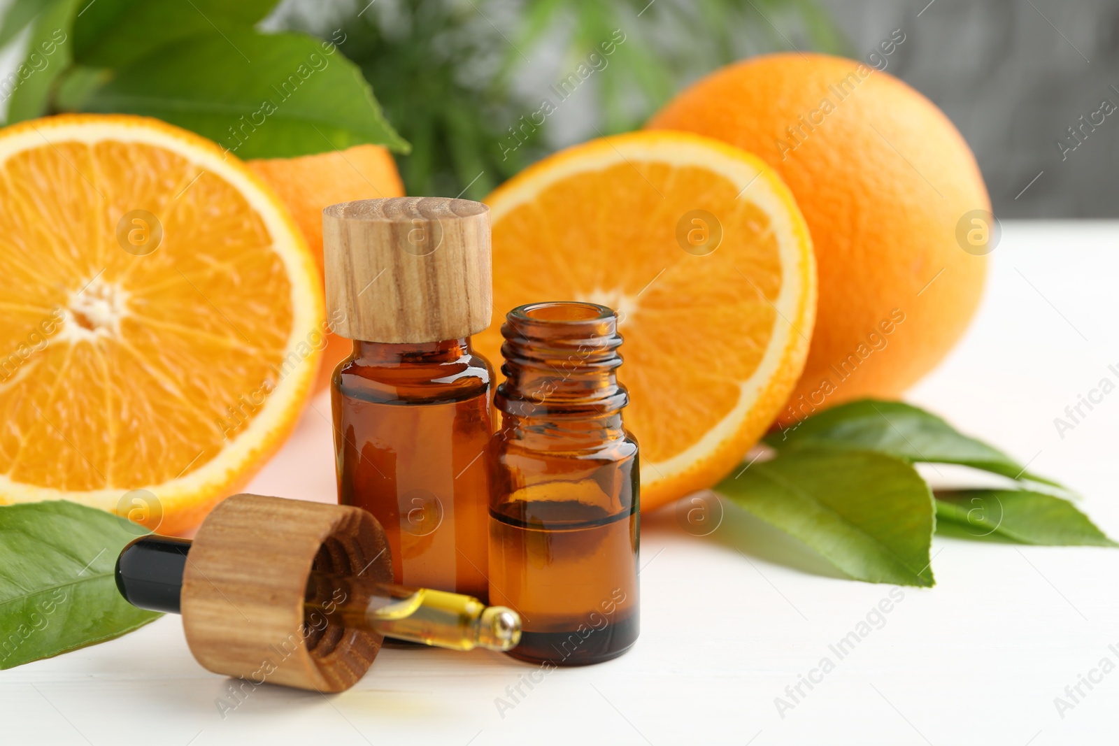 Photo of Essential oils in bottles, dropper, oranges and green leaves on white table