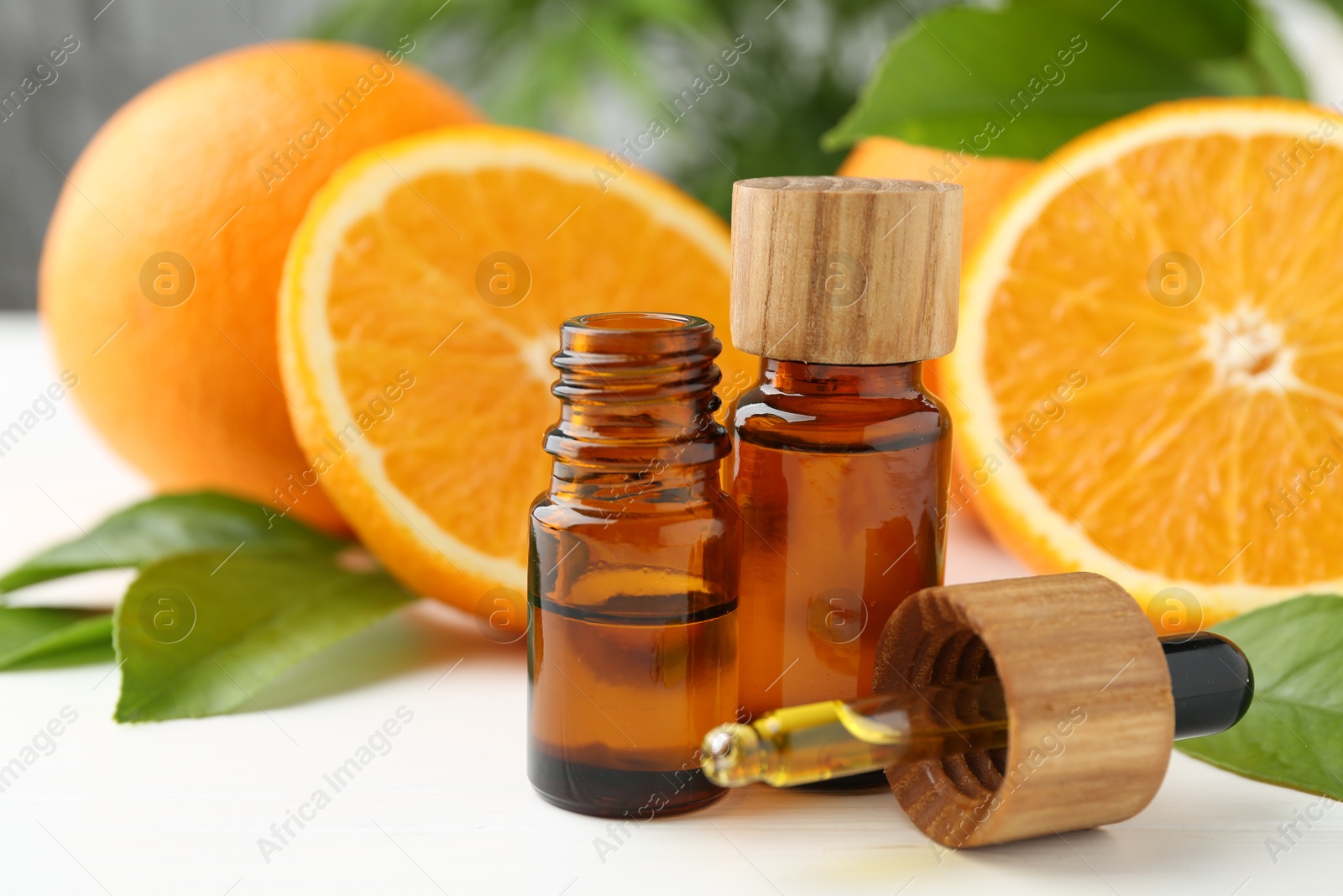 Photo of Essential oils in bottles, dropper, oranges and green leaves on white table, closeup