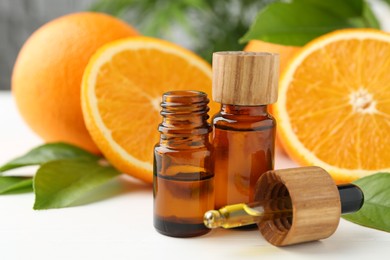 Photo of Essential oils in bottles, dropper, oranges and green leaves on white table, closeup