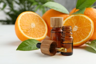 Essential oils in bottles, dropper, oranges and green leaves on white table