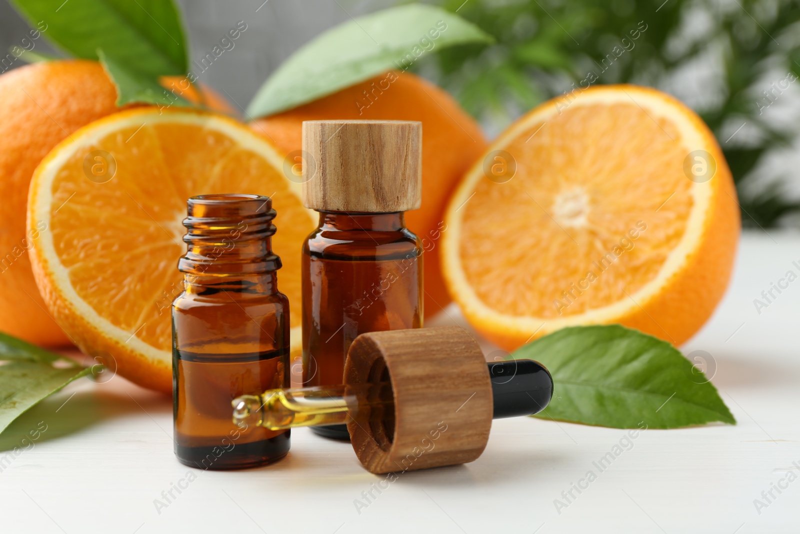 Photo of Essential oils in bottles, dropper, oranges and green leaves on white table