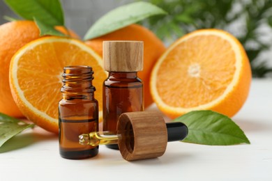 Essential oils in bottles, dropper, oranges and green leaves on white table