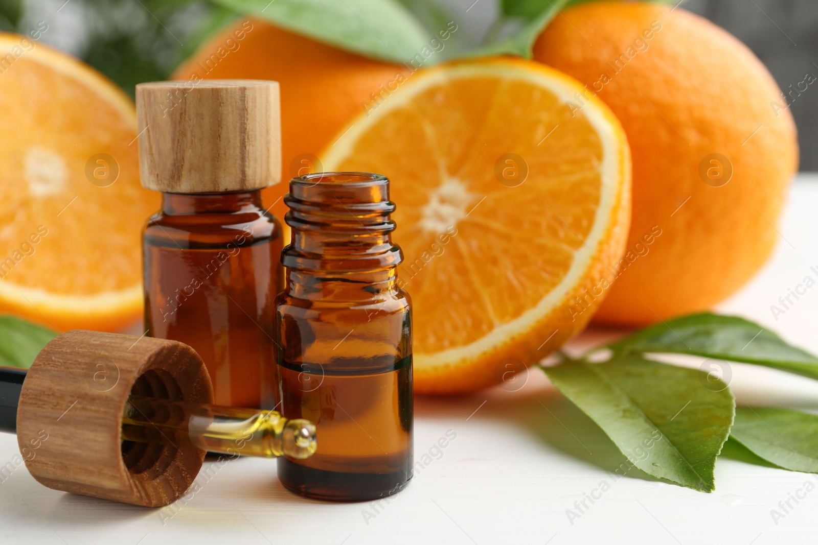 Photo of Essential oils in bottles, dropper, oranges and green leaves on white table, closeup