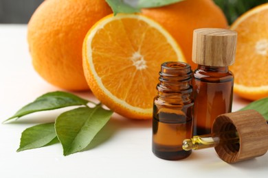 Essential oils in bottles, dropper, oranges and green leaves on white table, closeup