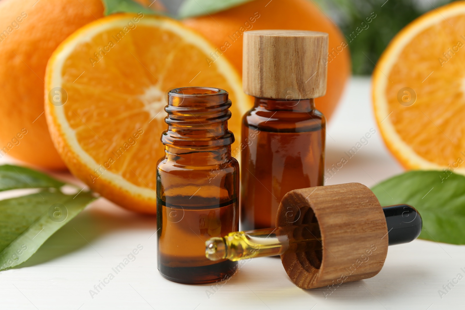 Photo of Essential oils in bottles, dropper, oranges and green leaves on white table, closeup