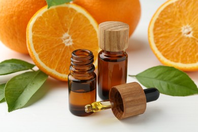 Essential oils in bottles, dropper, oranges and green leaves on white table