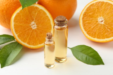 Essential oils in bottles, oranges and green leaves on white table