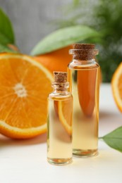 Essential oils in bottles and oranges on white table