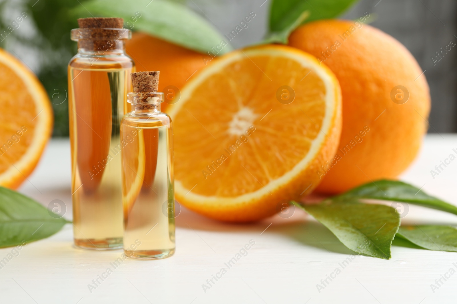 Photo of Essential oils in bottles, oranges and green leaves on white table