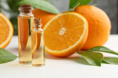 Essential oils in bottles, oranges and green leaves on white table