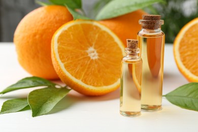 Photo of Essential oils in bottles, oranges and green leaves on white table