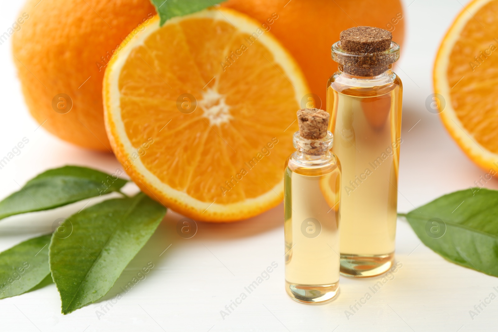 Photo of Essential oils in bottles, oranges and green leaves on white table, closeup