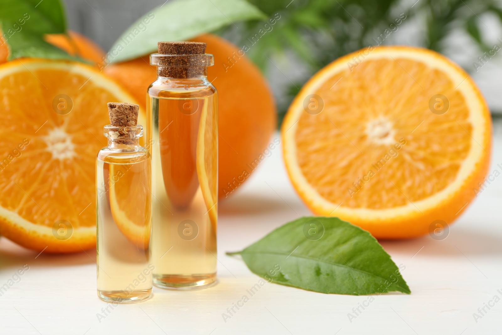 Photo of Essential oils in bottles, oranges and green leaves on white table, closeup