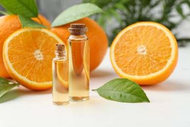 Essential oils in bottles, oranges and green leaves on white table