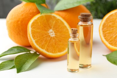 Photo of Essential oils in bottles, oranges and green leaves on white table, closeup