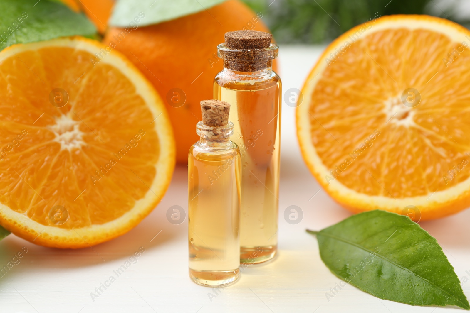 Photo of Essential oils in bottles, oranges and green leaves on white table, closeup