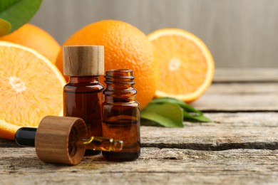 Essential oils in bottles, dropper, oranges and green leaves on wooden table. Space for text