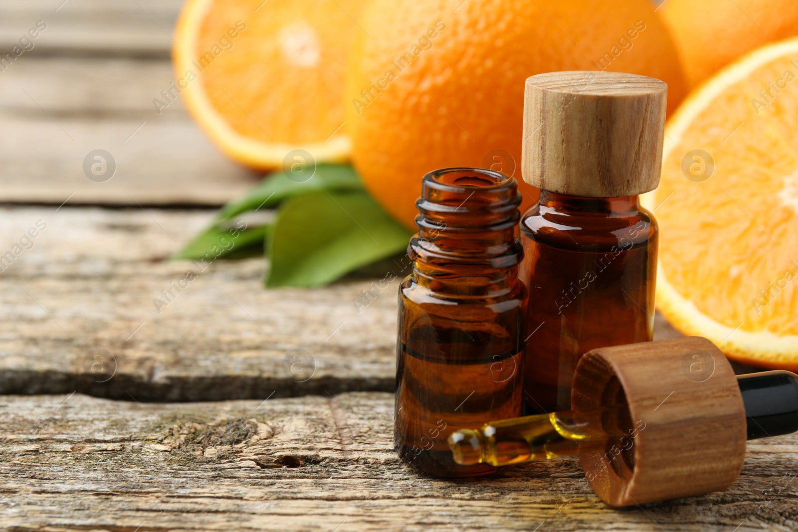 Photo of Essential oils in bottles, dropper, oranges and green leaves on wooden table, closeup. Space for text