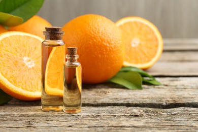 Essential oils in bottles, oranges and green leaves on wooden table. Space for text