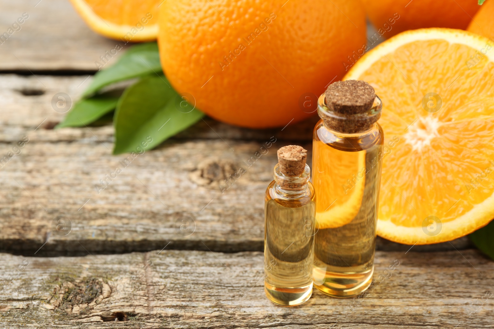 Photo of Essential oils in bottles, oranges and green leaves on wooden table. Space for text