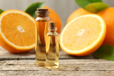 Photo of Essential oils in bottles, oranges and green leaves on wooden table, closeup