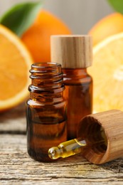 Photo of Essential oils in bottles, dropper and oranges on wooden table, closeup