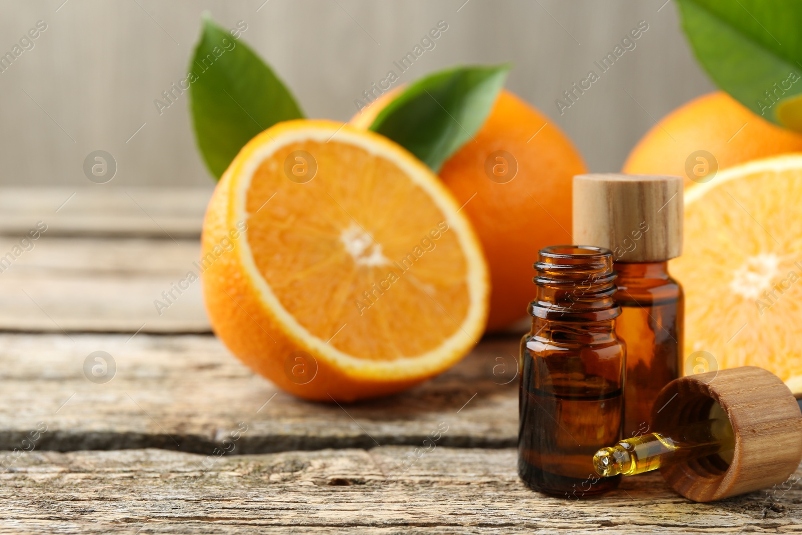 Photo of Essential oils in bottles, dropper, oranges and green leaves on wooden table