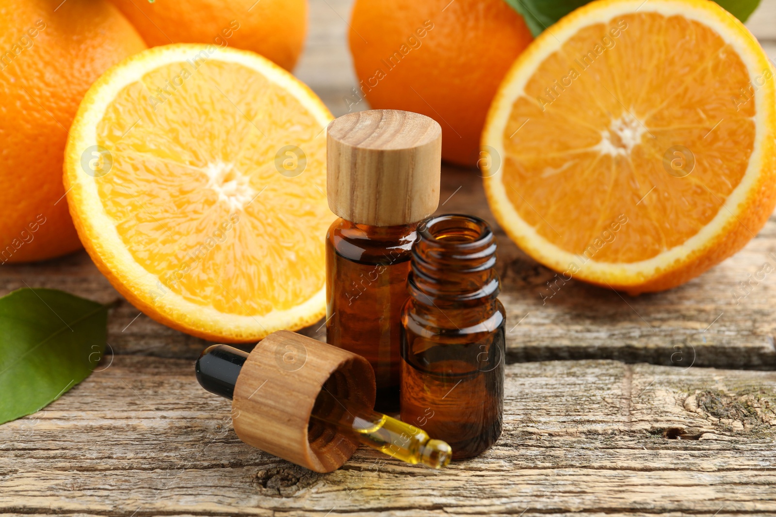 Photo of Essential oils in bottles, dropper, oranges and green leaf on wooden table