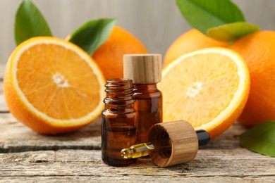 Essential oils in bottles, dropper, oranges and green leaves on wooden table