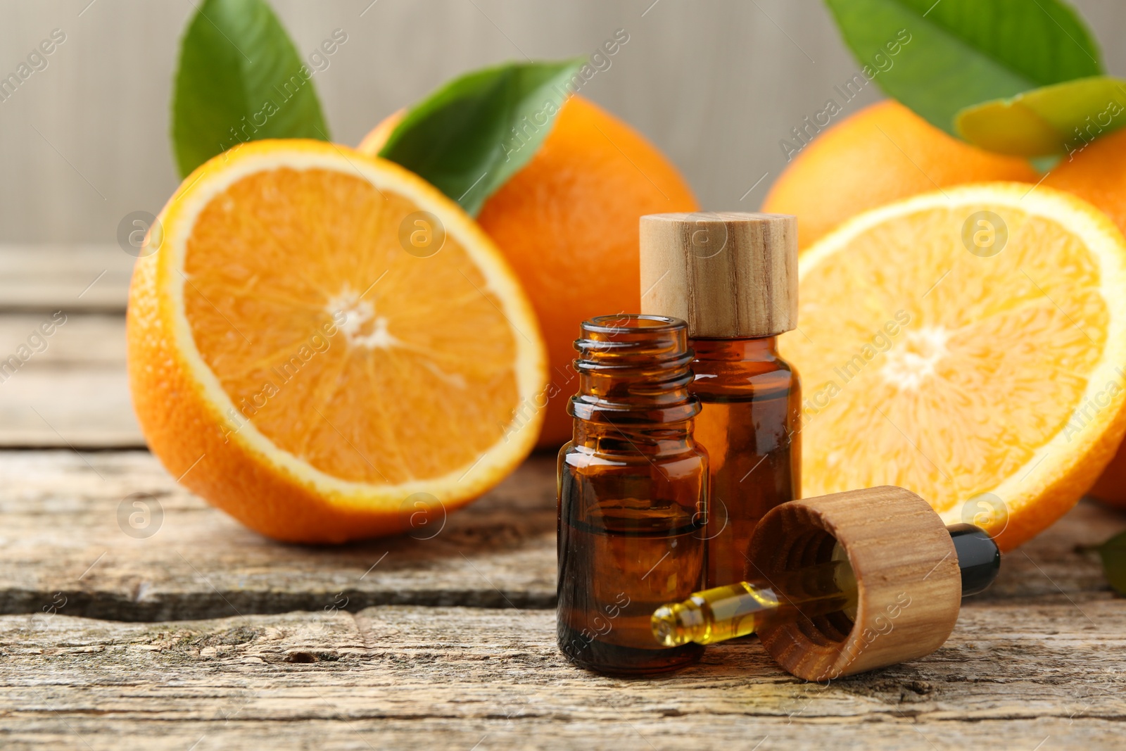 Photo of Essential oils in bottles, dropper, oranges and green leaves on wooden table