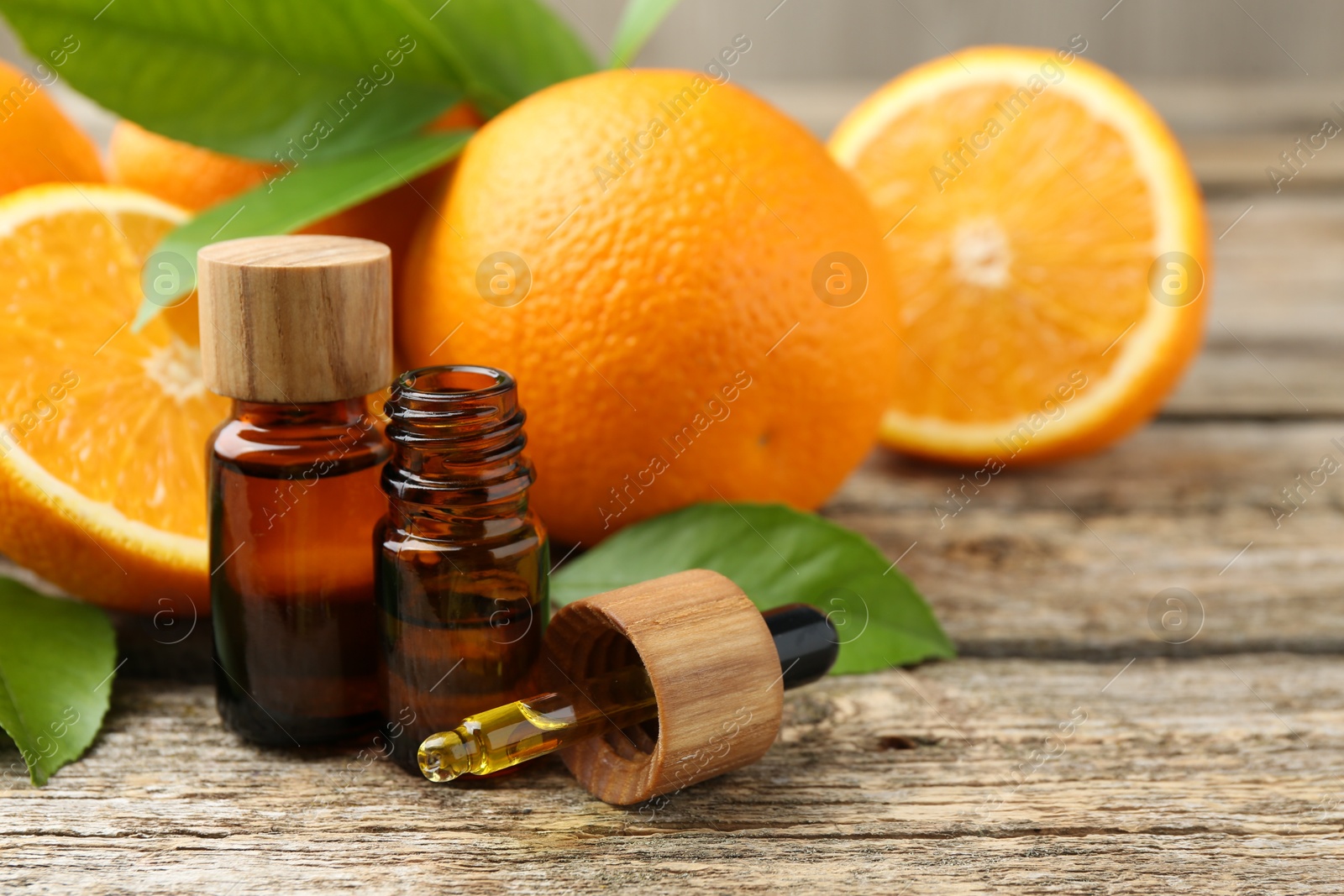 Photo of Essential oils in bottles, dropper, oranges and green leaves on wooden table