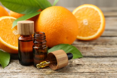 Photo of Essential oils in bottles, dropper, oranges and green leaves on wooden table