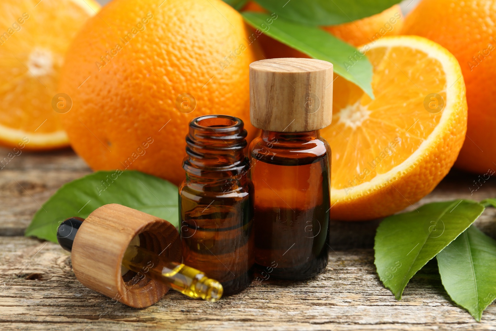 Photo of Essential oils in bottles, dropper, oranges and green leaves on wooden table, closeup