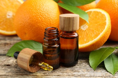 Photo of Essential oils in bottles, dropper, oranges and green leaves on wooden table, closeup