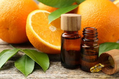 Essential oils in bottles, dropper, oranges and green leaves on wooden table, closeup