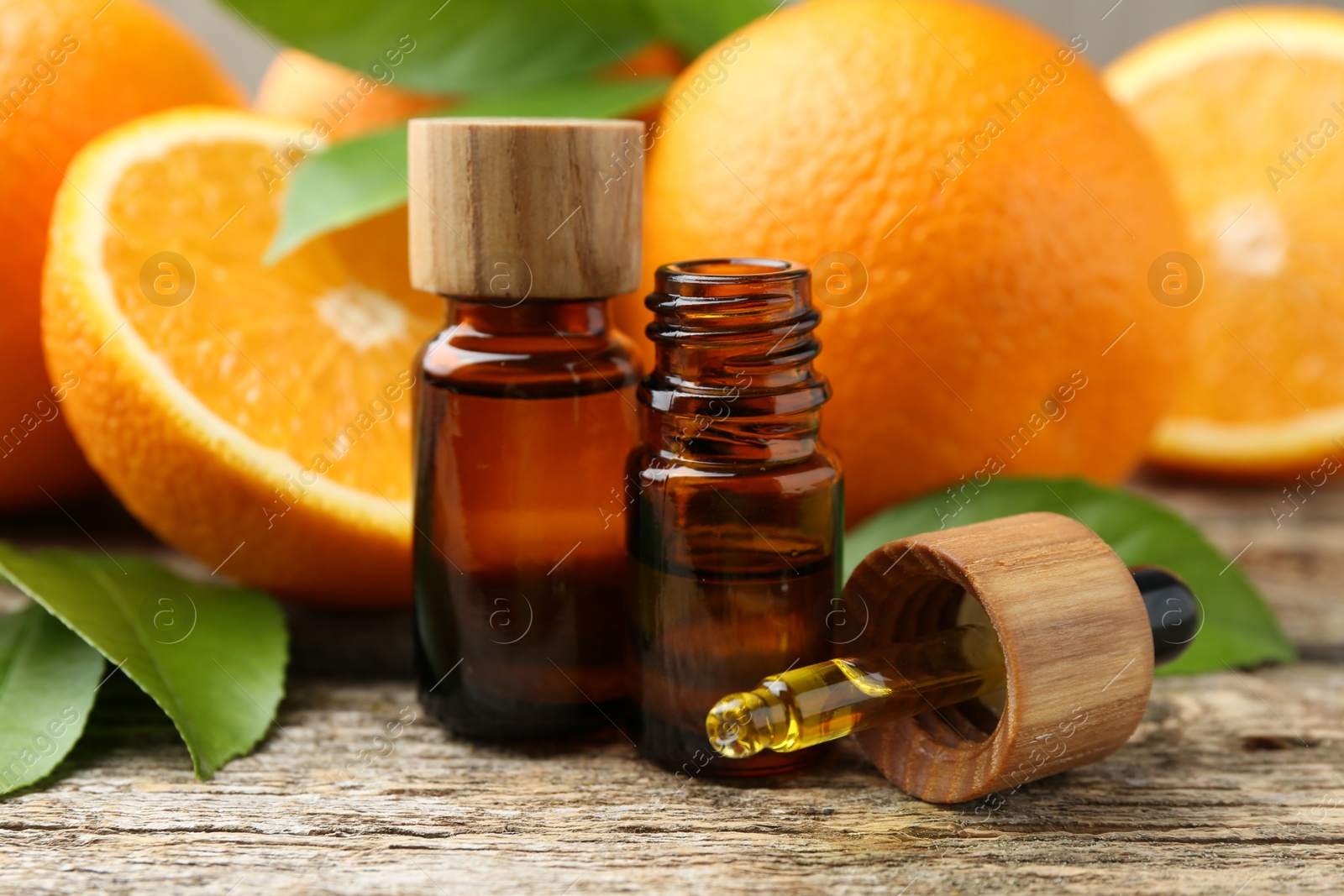 Photo of Essential oils in bottles, dropper, oranges and green leaves on wooden table, closeup