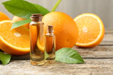 Photo of Essential oils in bottles, oranges and green leaves on wooden table