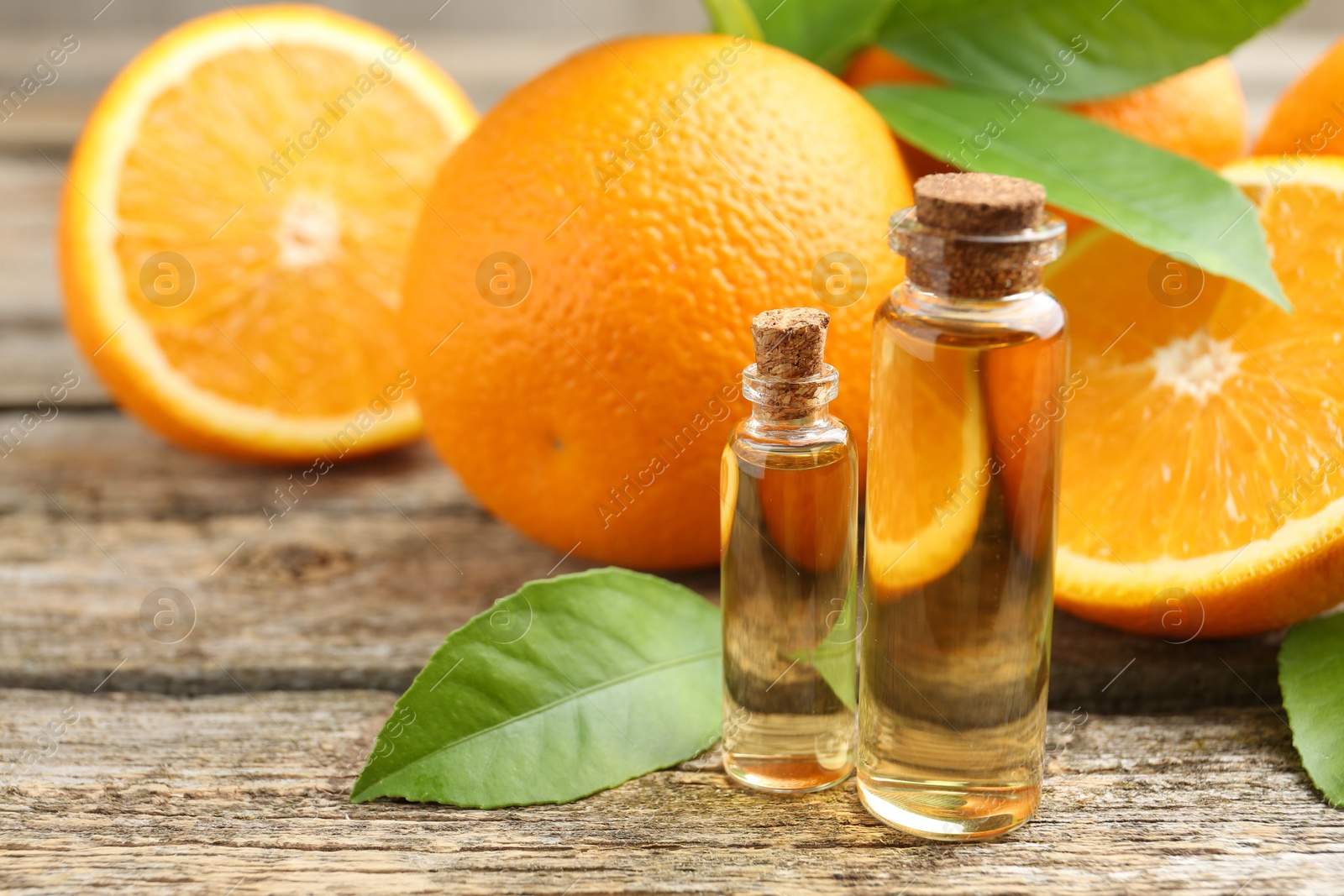 Photo of Essential oils in bottles, oranges and green leaves on wooden table, closeup